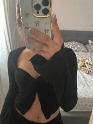 Svart croppad tröja - Snygg svart croppad topp med lång ärm. Toppen har en twistad detalj framtill och en djup v-ringning som ger en trendig look. Tillverkad i ett stretchigt syntetmaterial som sitter tight och bekvämt.