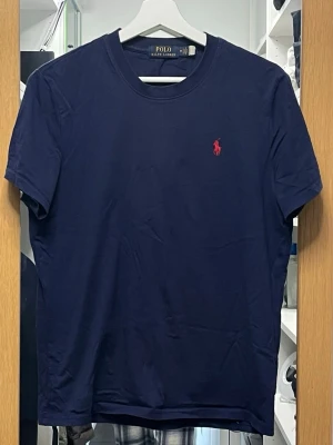 Mörkblå t-shirt från Polo Ralph Lauren - Klassisk mörkblå t-shirt från Polo Ralph Lauren med röd broderad logga. T-shirten har rund halsringning och korta ärmar. Tillverkad i mjuk bomull för en skön och avslappnad känsla. Passar S/M