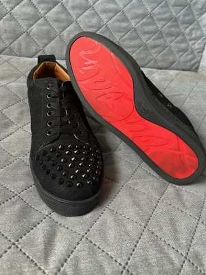 Louboutin skor - Snygga svarta sneakers från Christian Louboutin med mattsvarta nitar på tån och klassisk röd sula. Skorna har snörning, knappt använda