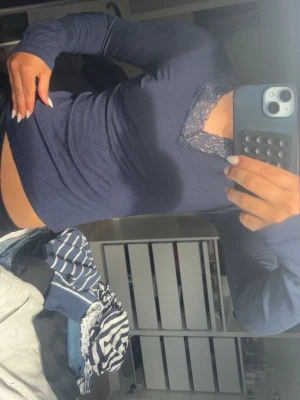 Mörkblå långärmad topp med spets - Mörkblå långärmad topp med v-ringning och dekorativ spetskant vid halsen. Tunn och stretchig modell som sitter tight mot kroppen. Perfekt att styla med jeans eller kjol för en trendig look.