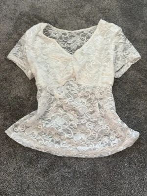 Vit spets babydoll med v-ringning - Säljer en söt vit babydoll i spets med v-ringad hals och korta ärmar. Babydollen har ett genombrutet spetsmönster som ger en romantisk vibe och är perfekt för att styla lager på lager. Passar dig som gillar feminina detaljer.