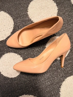 Nude pumps med spetsig tå - Snygga nude-färgade pumps med spetsig tå och smal klack. Skorna har en klassisk och elegant design i glansigt material som ger en stilren look. Perfekta för att lyfta vilken outfit som helst.