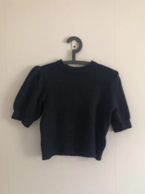 Mörkblå stickad tröja med puffärm - Mysig mörkblå stickad tröja med puffiga halvlånga ärmar och rund halsringning. Tröjan har en rak passform och är tillverkad i ett mjukt stickat material som känns skönt mot huden. Perfekt för dig som gillar en enkel men trendig look.
