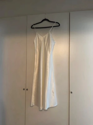 Klänning i 100% silke  - Elegant vit långklänning med smala axelband och v-ringad hals. Klänningen har en slät, glansig yta i silke!🌸☺️ Den är i bra skick, men har mindre defekter (dragning samt axelband), se bilder.