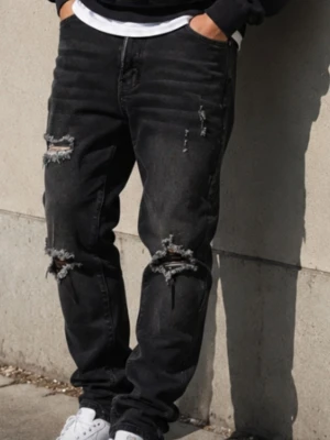 Svarta ripped jeans med relaxed fit - Säljer ett par svarta jeans med slitna detaljer och stora hål vid knäna. Jeansen har relaxed fit, fem fickor och är tillverkade i denim. Perfekta för en streetwear-look och passar dig som gillar en avslappnad stil.