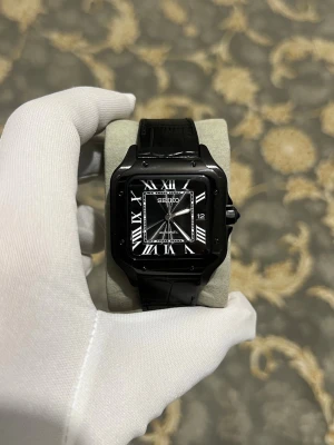 Svart Seiko Santos - Stilren svart klocka från Seiko med fyrkantigt ur och romerska siffror på urtavlan. Klockan har svart läderarmband och automatisk urverk som syns genom baksidan. Klassisk och elegant design med vita detaljer på urtavlan.