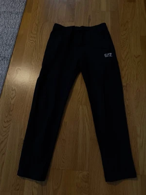 Svarta mjukisbyxor från EA7 Armani - Säljer ett par svarta mjukisbyxor från EA7 Emporio Armani. Byxorna har en avslappnad passform, resår i midjan med dragsko och diskret EA7-logga på vänster sida. Perfekta för chill dagar eller när du vill ha en clean look.