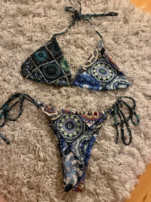 Utomlands Mönstrad trekantsbikini med knyt - Snygg trekantsbikini med färgstarkt blommönster i blått, grönt och vitt. Både överdel och underdel har knytband i sidorna och nacken för justerbar passform. Perfekt för sommardagar på stranden eller poolen.