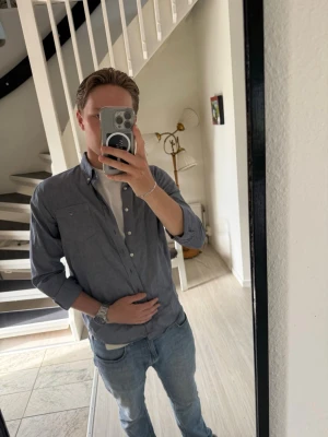 Blå skjorta i bomull med knappar - Snygg blå skjorta med klassisk krage och knappar framtill. Skjortan är långärmad och har en avslappnad passform. Perfekt att bära över en t-shirt för en casual look. Tillverkad i mjuk bomull som känns skön mot huden.
