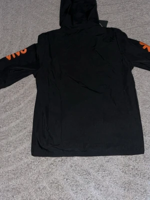 Nike Brasil GORE-TEX vindjacka svart - Snygg svart vindjacka från Nike med Brasil-logga och flera sponsortryck i gult och orange. Jackan har huva, hel dragkedja och är tillverkad i GORE-TEX-material som står emot regn och vind. Perfekt för dig som gillar sportig stil och vill sticka ut.