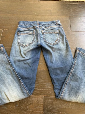 Blå bootcut jeans från nelly - Säljer ett par blå bootcut jeans med snygga tvättade detaljer. Klassisk femficksmodell med knapp och dragkedja fram. Jeansen har kontrastsömmar och är tillverkade i denim, perfekt för en avslappnad och trendig look.