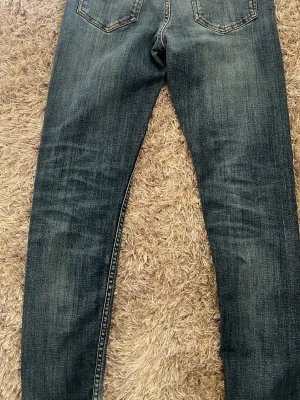 Blå raka jeans med slitningar - Säljer ett par klassiska blå jeans med raka ben och snygga slitningar. Jeansen har fem fickor och normal midja. 29/32, nästan helt nya 
