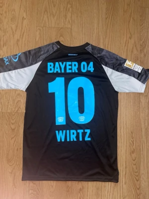 Bayer Leverkusen Wirtz matchtröja - Snygg svart Bayer 04 Leverkusen matchtröja från Castore med Wirtz och nummer 10 på ryggen. Tröjan har ljusblå detaljer, klubbmärke och sponsortryck på bröstet samt tryck på ärmarna. Tillverkad i lätt och ventilerande funktionsmaterial.