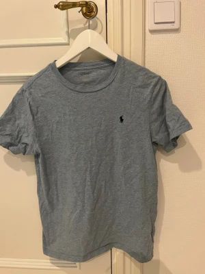 Ljusblå t-shirt från Ralph Lauren - Klassisk ljusblå t-shirt från Ralph Lauren med den ikoniska lilla loggan broderad på bröstet. T-shirten har rund halsringning och korta ärmar. Tillverkad i mjuk bomull för en skön och avslappnad stil.