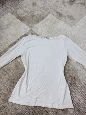 Vit långärmad topp från 157 - En basic vit långärmad topp från 157 med rund halsringning. Tunn och mjuk i materialet, perfekt att ha som lager eller till jeans. Enkel och stilren design som funkar till många olika looks.