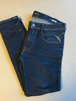 Replay anbass - Snygga mörkblå jeans från Replay med klassisk femficksdesign och diskreta slitningar. Jeansen har en smal passform och detaljer som ljusblå knapp och logotyp på fickan. Perfekta för en trendig och avslappnad look.  W32 L30. Minimalt slitna i skrevet men syns inte vid användning