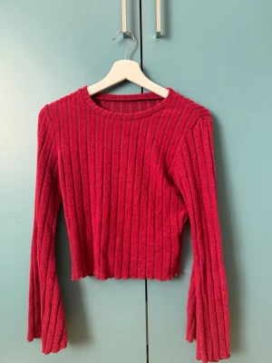 Tröja  - Trendig röd stickad tröja med breda ribbor och vida, långa ärmar. Croppad modell med rund halsringning. Perfekt för dig som vill ha en statement piece i garderoben. Materialet känns mjukt och stretchigt.