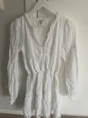 Sommarklänning från Nelly - Superfin vit kort klänning från Nelly med broderade spetsdetaljer och v-ringning. Klänningen har långa ärmar och markerad midja, perfekt för sommarens alla tillfällen. 