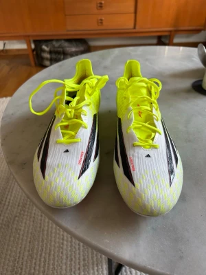 Adidas F50 Elite AG/FG fotbollsskor - Säljer ett par Adidas F50 AG/FG fotbollsskor i vitt och neongult med svarta och röda detaljer. Säljer de eftersom skorna inte kommer till användning. Jag har använt skorna 1 träning, så nytt skick.