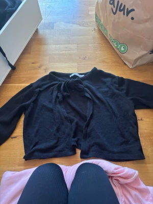 Svart knytkofta från 157 - Säljer en svart kofta från 157 med knytning framtill. Koftan har långa ärmar och är gjord i ett mjukt, tunt material som passar perfekt till lager på lager. Enkel och stilren design som är lätt att matcha med olika outfits.