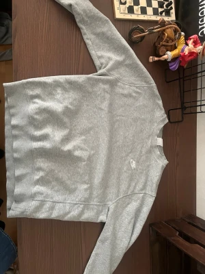 Grå sweatshirt från Nike - Snygg grå sweatshirt från Nike med diskret logga på bröstet. Tröjan har rund halsringning och långa ärmar. Tillverkad i mjukt bomullsmaterial som känns skönt mot huden. Perfekt för en avslappnad och sportig stil.