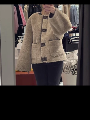 Beige teddyjacka med stora knappar - Mysig beige teddyjacka med breda ärmar och stora bruna knappar framtill. Jackan har två stora fickor och är tillverkad i fluffigt teddy-material som ger en cool och avslappnad look. Perfekt för dig som gillar trendiga och bekväma plagg.Säljs för 1500 kr. 