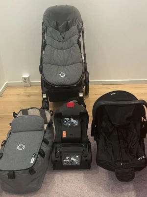 Bugaboo barnvagn med tillbehör - Säljer en grå Bugaboo barnvagn med matchande liggdel, babyskydd från BeSafe och en svart bilbas. Vagnen har stora hjul och justerbart handtag. Perfekt för småbarnsföräldrar som vill ha allt i ett paket.