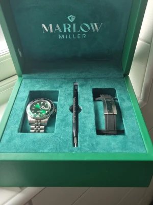 Grön och silver klocka Marlow Miller - Snygg klocka från Marlow Miller med grön urtavla och silverfärgad länk i metall. Kommer i originalbox med extra svart armband och verktyg för byte. Perfekt accessoar för dig som vill sticka ut med stilren design.