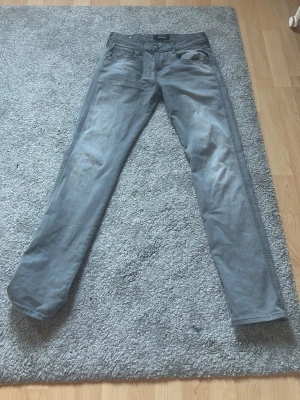 Grå slim fit jeans från Replay - Snygga grå slim fit jeans från Replay med klassisk femficksdesign och dragkedjegylf. Jeansen har en lätt tvättad look och är tillverkade i stretchigt denimtyg för extra komfort. Perfekta för en trendig och avslappnad stil. Storlek 30/32. Använda max 5 gånger