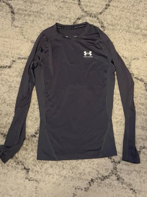  Långärmad träningströja Under armour - Snygg svart långärmad träningströja från Under Armour med diskret logga på bröstet. Tillverkad i ett stretchigt funktionsmaterial som andas och sitter tight mot kroppen. Perfekt för gymmet eller löprundan.