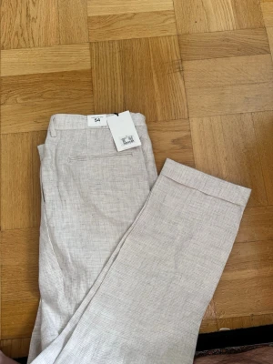 Beige linnebyxor med pressveck Helt ny och oanvänd med prislapp kvar. - Snygga beige linnebyxor från Glory days med diskret rutmönster, pressveck och uppvikta benslut. Byxorna har passpoalfickor bak och bälteshällor i midjan. Perfekta för en stilren och avslappnad look.Helt ny och oanvänd med prislapp kvar.