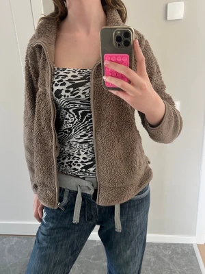 Beige teddyjacka med dragkedja - Mysig teddyjacka i beige färg med hög krage och dragkedja framtill. Jackan har ribbade detaljer vid nederkant och ärmslut samt snörning i midjan. Perfekt för att hålla sig varm och stilen är avslappnad och trendig. Den är välanvänd+ förliten för mig!(Mer en kofta än jacka) 