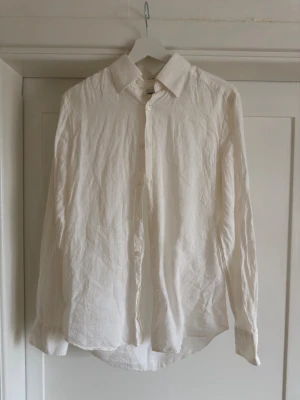 Vit linneskjorta från These Glory Days - Klassisk vit skjorta i 100% linne från These Glory Days. Slim fit-modell med långa ärmar och knappar framtill. Perfekt för en clean och stilren look, lätt och luftig känsla tack vare linnematerialet.
