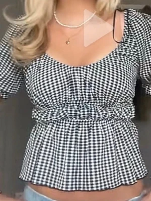 Rutig svartvit blus  - Supersöt blus i svartvitt rutigt mönster med korta puffärmar och markerad midja. Toppen har en lätt v-ringad urringning och volangkant nedtill. Perfekt för dig som gillar trendiga och feminina detaljer.
