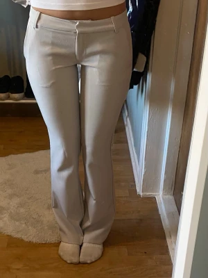 Ljusgrå kostymbyxor bootcut - Snygga ljusgrå kostymbyxor med bootcut-modell och pressveck. Byxorna har hällor för skärp, två fuskfickor bak och stängs med dragkedja och hake. Perfekta för en clean och stilren look.