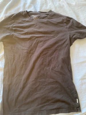 Svart t-shirt från Jack & Jones - En stilren svart t-shirt från Jack & Jones med rund halsringning och diskret logga på bröstet. T-shirten är i mjuk bomull och har en klassisk passform med korta ärmar. Perfekt basplagg till garderoben.