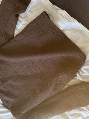 Brun mönstrad tröja med struktur - Säljer en brun tröja med upphöjt geometriskt mönster över hela plagget. Tröjan har rund halsringning och långa ärmar med ribbade muddar. Materialet känns mjukt och stretchigt, perfekt för dig som gillar stilrena detaljer.
