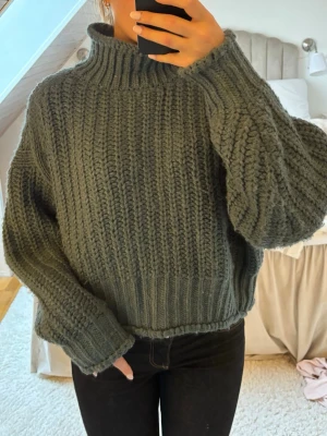 Grå chunky stickad polotröja - Mysig och oversized stickad tröja i mörkgrått med hög krage och grov ribbstickning. Tröjan har långa ärmar och avslappnad passform, perfekt för kalla dagar. Materialet känns mjukt och värmande.