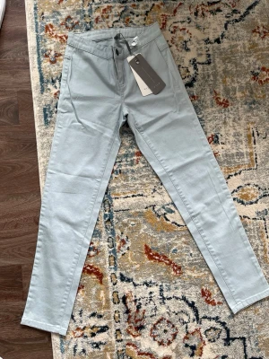 Ljusgrå chinos från VILA - Snygga ljusgrå chinos från VILA med klassisk rak passform och normal midja. Byxorna har framfickor och bälteshällor, perfekta för en stilren look. Tillverkade i ett mjukt och bekvämt bomullsmaterial med lite stretch för extra komfort.