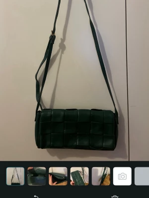Mörkgrön axelväska i flätad läderlook - Säljer denna mörkgröna axelväska med justerbar rem och flätad design. Väskan har en rektangulär form och stängs med magnetlås. Säljer pågrund av den inte kommer till användning, skriv om du har frågor eller nåt!