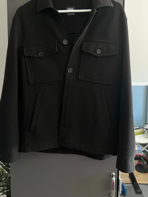 Svart overshirt från Zara - Stilren svart overshirt från Zara med klassisk krage, två stora bröstfickor med lock och knappar. 