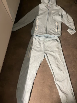 Ljusblå NOCTA x Nike loungewear set - Säljer ett ljusblått loungewear set från NOCTA x Nike. Setet består av en hoodie med dragkedja och två fickor samt matchande byxor med resår i midjan och fickor. Båda delarna har diskreta Nike-loggor. Perfekt för chill dagar hemma.