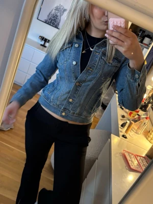 Klassisk blå jeansjacka - Snygg blå jeansjacka med klassisk passform och silverfärgade knappar. Jackan har två bröstfickor med lock och knappar samt två sidofickor. Perfekt att slänga över en t-shirt eller hoodie för en avslappnad look.