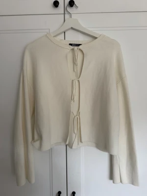 Vit kofta med knytning från Gina Tricot - Trendig vit kofta från Gina Tricot med tre knytband framtill. Koftan har lång ärm, rak passform och är tillverkad i ett mjukt stickat material. Perfekt att slänga över en topp för en avslappnad look.