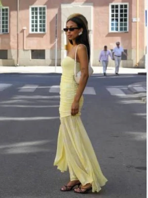 Ljusgul axelbandslös långklänning - Snygg axelbandslös långklänning i ljusgul nyans med figurnära passform och lätt transparent nederdel. Klänningen har en draperad effekt över kroppen och är tillverkad i ett tunt, flowy material som ger en elegant siluett.