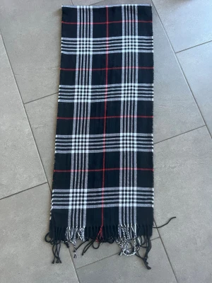 Svartvit rutig halsduk med fransar - Snygg halsduk i svart, vitt och rött med klassiskt rutmönster och fransar i ändarna. Perfekt accessoar för att lyfta din outfit och hålla dig varm. Mjuk och skön känsla, passar till det mesta. Pris går att diskuteras