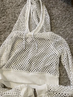 Vit mesh hoodie med huva - Säljer en vit hoodie i meshmaterial med stora hål och ribbade muddar. Hoodien har dragsko i huvan och är perfekt för en sportig och trendig look. Passar dig som gillar streetstyle och vill sticka ut lite extra.