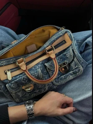 Louis Vuitton denim handväska - Trendig handväska från Louis Vuitton i blått denimtyg med klassiskt monogrammönster och detaljer i ljust läder. Väskan har två framfickor med spännen, dragkedja upptill och korta handtag. Perfekt accessoar för en cool streetstyle-look. Så himla himla snygg! Första två bilderna är lånade, väskan är använd men alla dragkedjor etc funkar precis som de ska!🩷