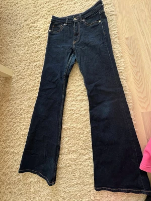 Mörkblå bootcut jeans - Snygga mörkblå bootcut jeans med klassisk femficksmodell och kontrastsömmar. Jeansen har hög midja och vida ben, perfekta för en trendig och avslappnad stil. Tillverkade i denim med stretch för extra komfort.