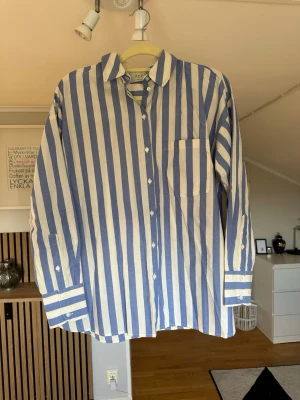 Blåvit randig skjorta från Adpt - Snygg skjorta från Adpt med breda blå och vita ränder. Skjortan har klassisk krage, bröstficka och knäppning framtill. Tillverkad i bomull och har långa ärmar med knappar vid manschetterna. Perfekt för en stilren look.